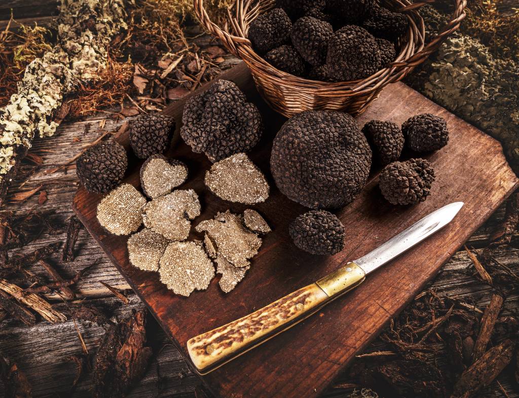 Black truffle with knife over rustic wooden cutting board